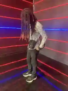 Prince Jona in a patterned shirt and black trousers under red and blue neon lights