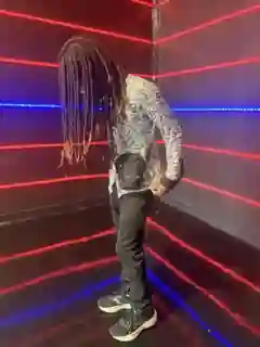 Second angle of Prince Jona with locs hanging forward in the same red-and-blue light