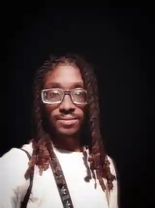 Prince Jona smiling in glasses against a nearly black background
